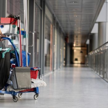 An employee pulls a trolley for cleaning offices. Woman cleaner is engaged in work. An employee pulls a trolley for cleaning offices. Woman cleaner is engaged in work. Shopping center place for text